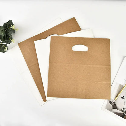 Die-cut kraft bag flat folded brown and white sacks showing creased base and punch handle