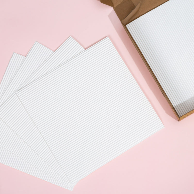 Fluted pizza liner square sheets fanned out and stacked inside carton